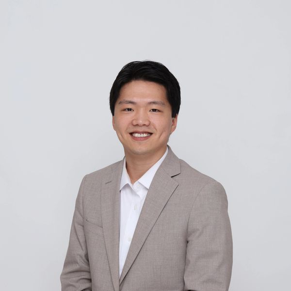 Young man in a beige suit smiling.