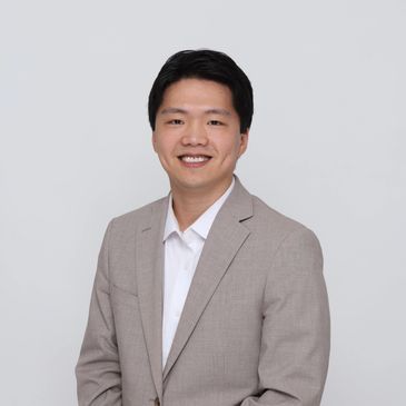 Smiling man in a beige suit jacket and white shirt against a plain background.