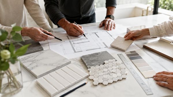 People discussing architectural plans with tile and color samples on a marble table.