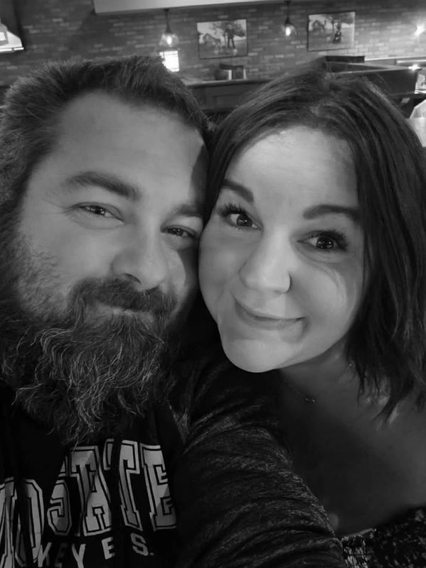 Close-up black and white selfie of a smiling couple in a cozy setting.