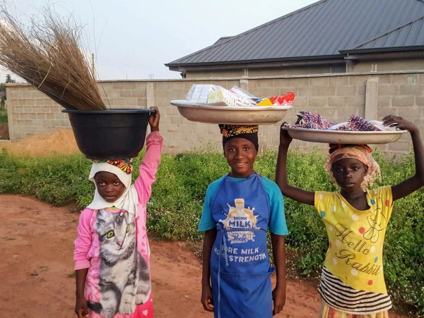 Three children carrying baskets on their heads outside.