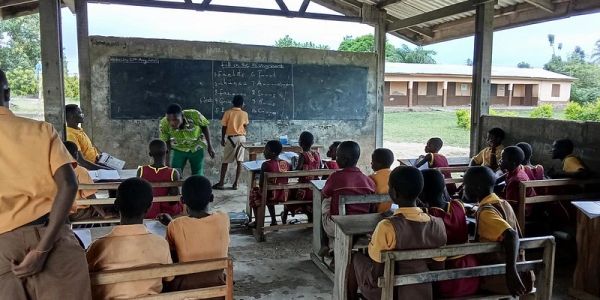 Outdoor classroom with students and teacher at a blackboard.