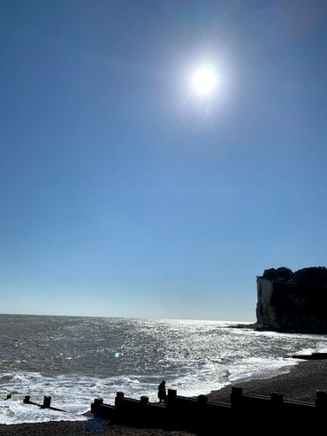 Bright sun over a rocky beach with waves crashing.