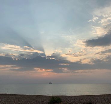 Sun rays piercing through clouds over a calm sea at sunset.