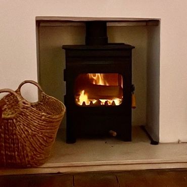 Cozy wood-burning stove with fire inside and a wicker basket nearby.