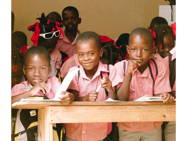 Three young boys in pink shirts smiling at school behind a wooden desk.