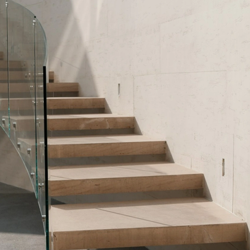 Modern beige stone staircase with glass railing and shadow play.