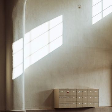 Sunlight casts geometric shadows on a minimalist wall with a small cabinet.