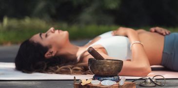 Woman relaxing on a yoga mat with meditation tools nearby.