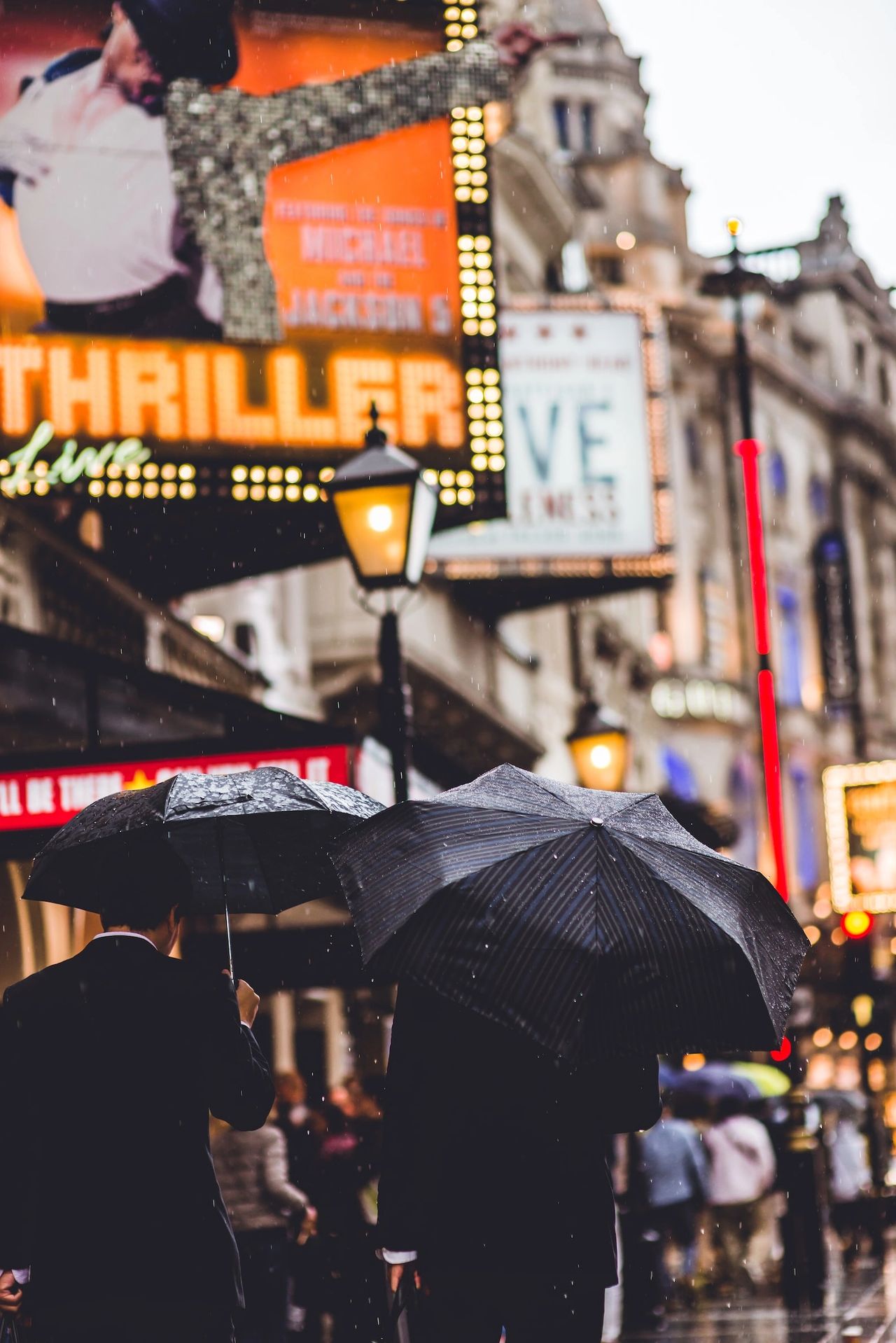 2 men walking in a rainy London West End with umbrellas 