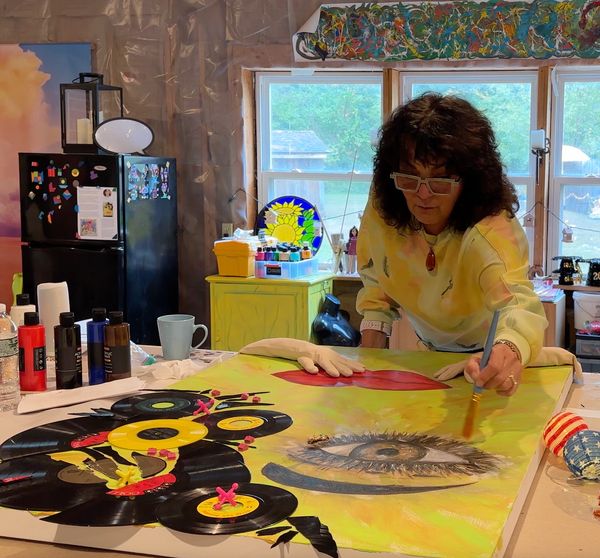 Woman painting a colorful artwork with a large eye and vinyl records in a cozy studio.