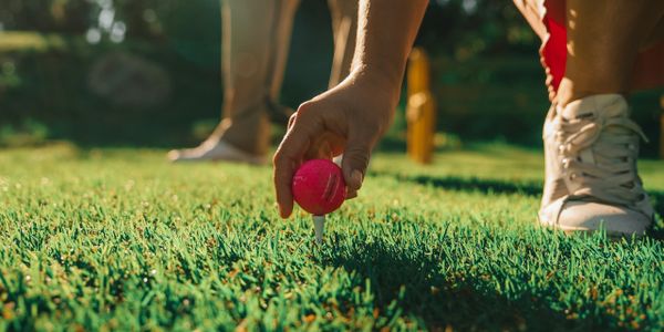 Person placing a pink golf ball on a tee on a sunny golf course.