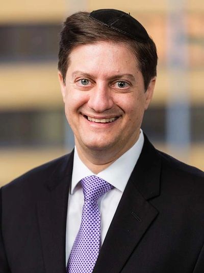 Smiling man in suit with a purple tie and black yarmulke.