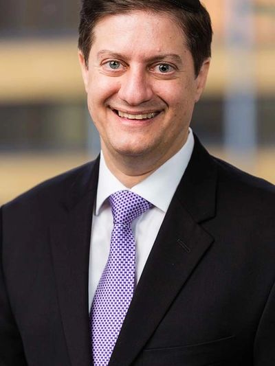 Smiling man in suit with a purple tie and black yarmulke.