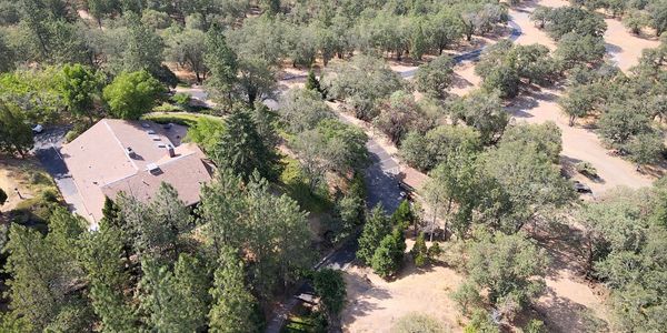 Aerial view of a large house surrounded by dense trees and winding roads.