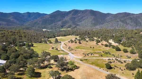 Scenic countryside with winding roads and forested mountains under a clear blue sky.