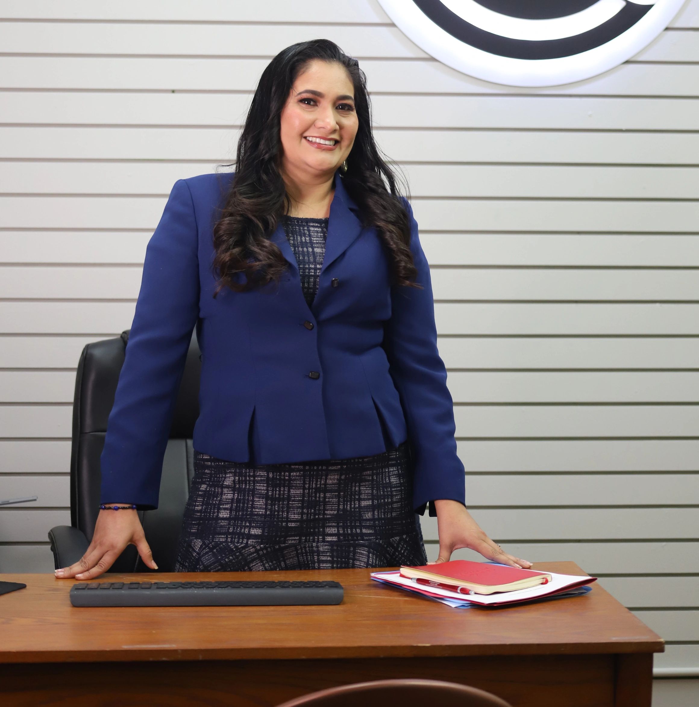 Smiling businesswoman standing at desk with files and keyboard.
