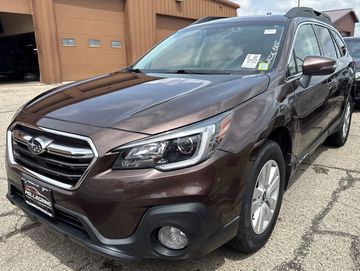 Brown Subaru Outback parked near a building on a sunny day.