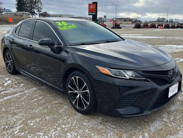 Black 2020 Toyota Camry sedan parked on a gravel lot with snow patches.