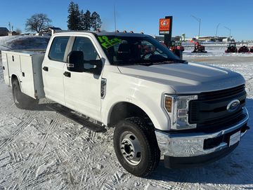 White Ford utility truck parked on snowy ground under clear blue sky.