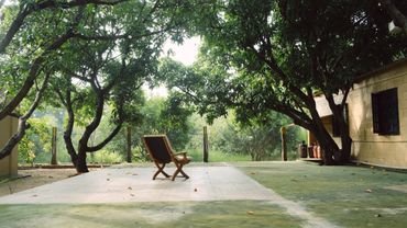 A single chair on a concrete patio surrounded by lush trees and greenery.