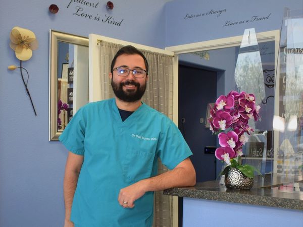 A smiling man in teal scrubs standing by a reception counter with a purple orchid.