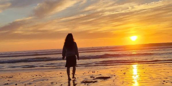 a photo of Alicia from the back walking on the beach during sunset