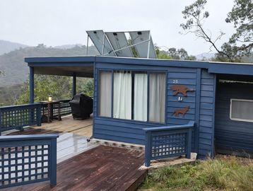 Blue cabin with solar panels in a mountainous, forested area.