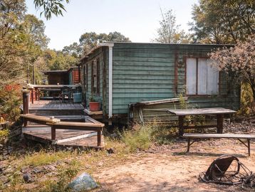 Old green wooden cabin with a deck in a rustic outdoor setting.