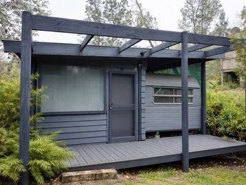 Small modern cabin with dark blue exterior and wooden porch.