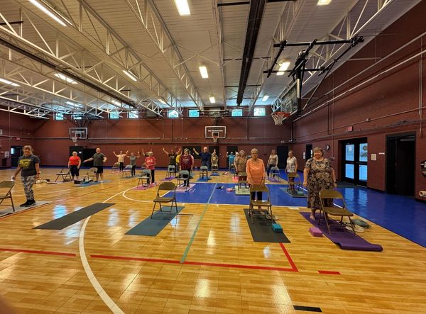 Group of seniors exercising with chairs in a gymnasium.