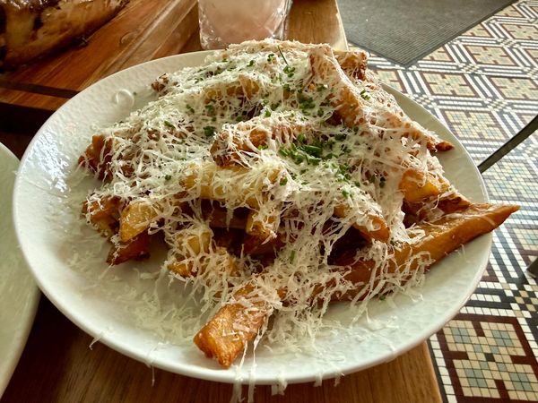 image of hand-cut french fries in a white dish with grated Pecorino Romano cheese and chives on top.