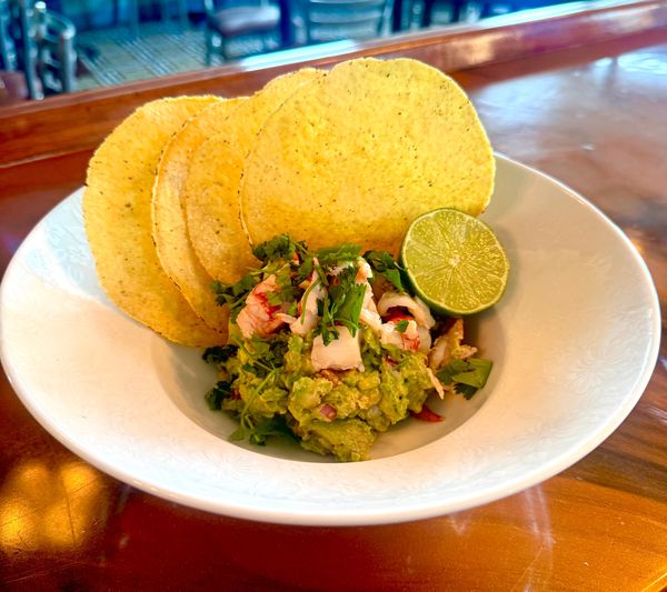 birds eye view fresh chunky green guacamole with large corn tostadas in a white bowl with halved lim