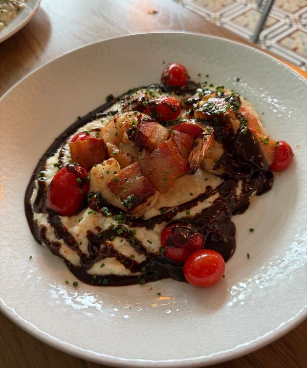 close up of shrimp and grits entree with large bacon pieces, and swirls of BBQ sauce