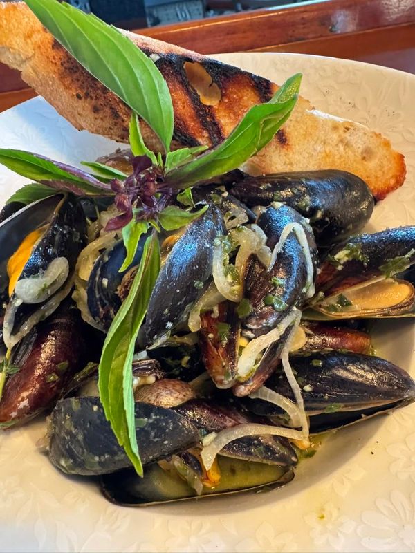 close up of steamed mussels, Thai basil garnish, and bread
