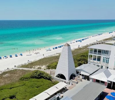 Beach with turquoise water, umbrellas, and a unique white tower structure.