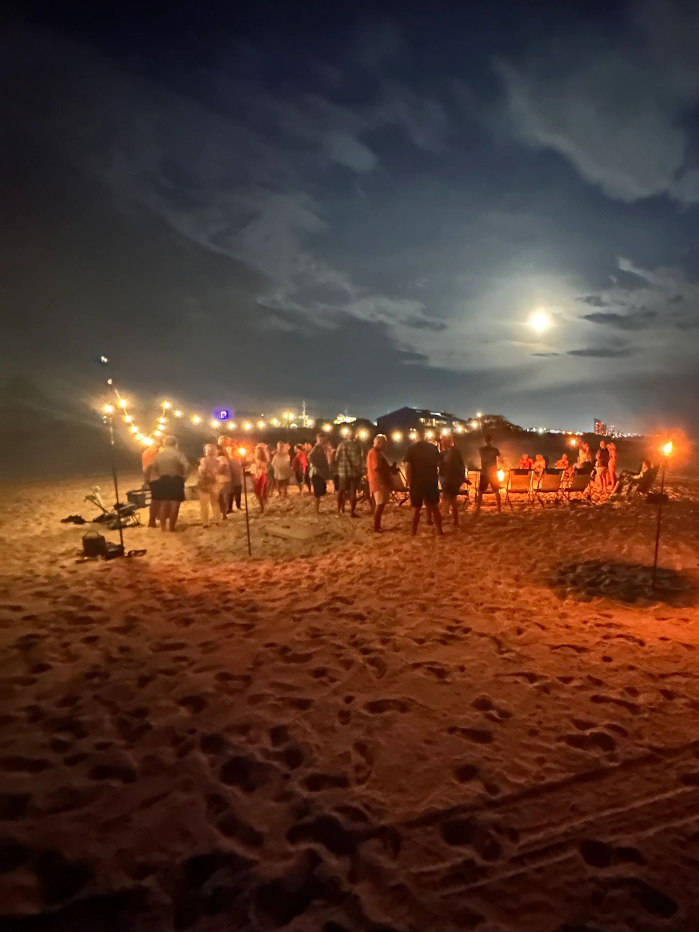 Beach party with string lights and fire torches at night.