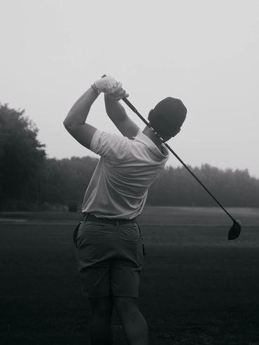 Golfer swinging a club on a misty course.