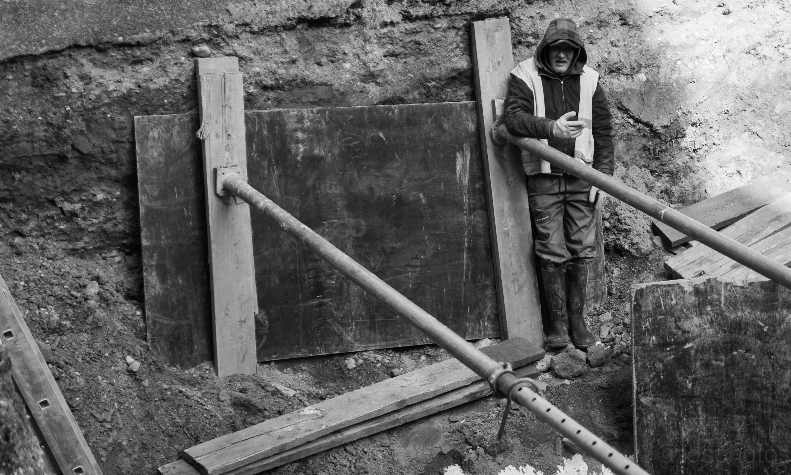 Construction worker standing in a trench with support beams.
