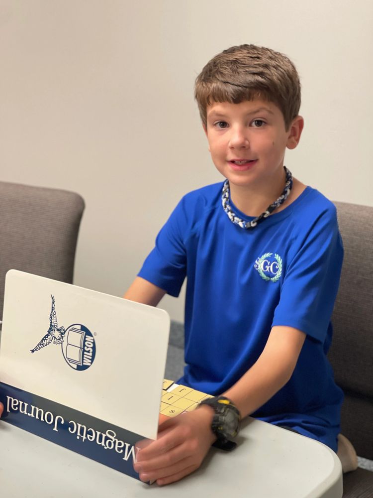A boy in a blue shirt holding a Wilson Magnetic Journal at a white table.