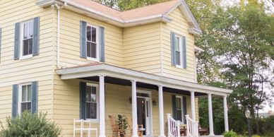 Yellow two-story house with white porch and rocking chairs.
