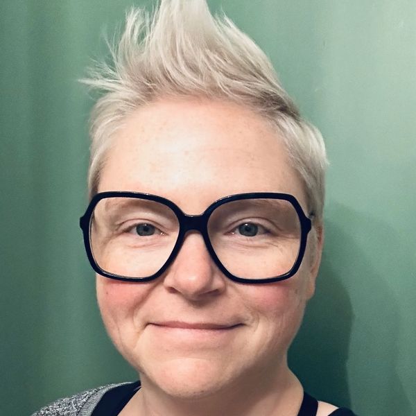 Image of Bren Thompson, blonde short spiky hair, green eyes, large square black glasses