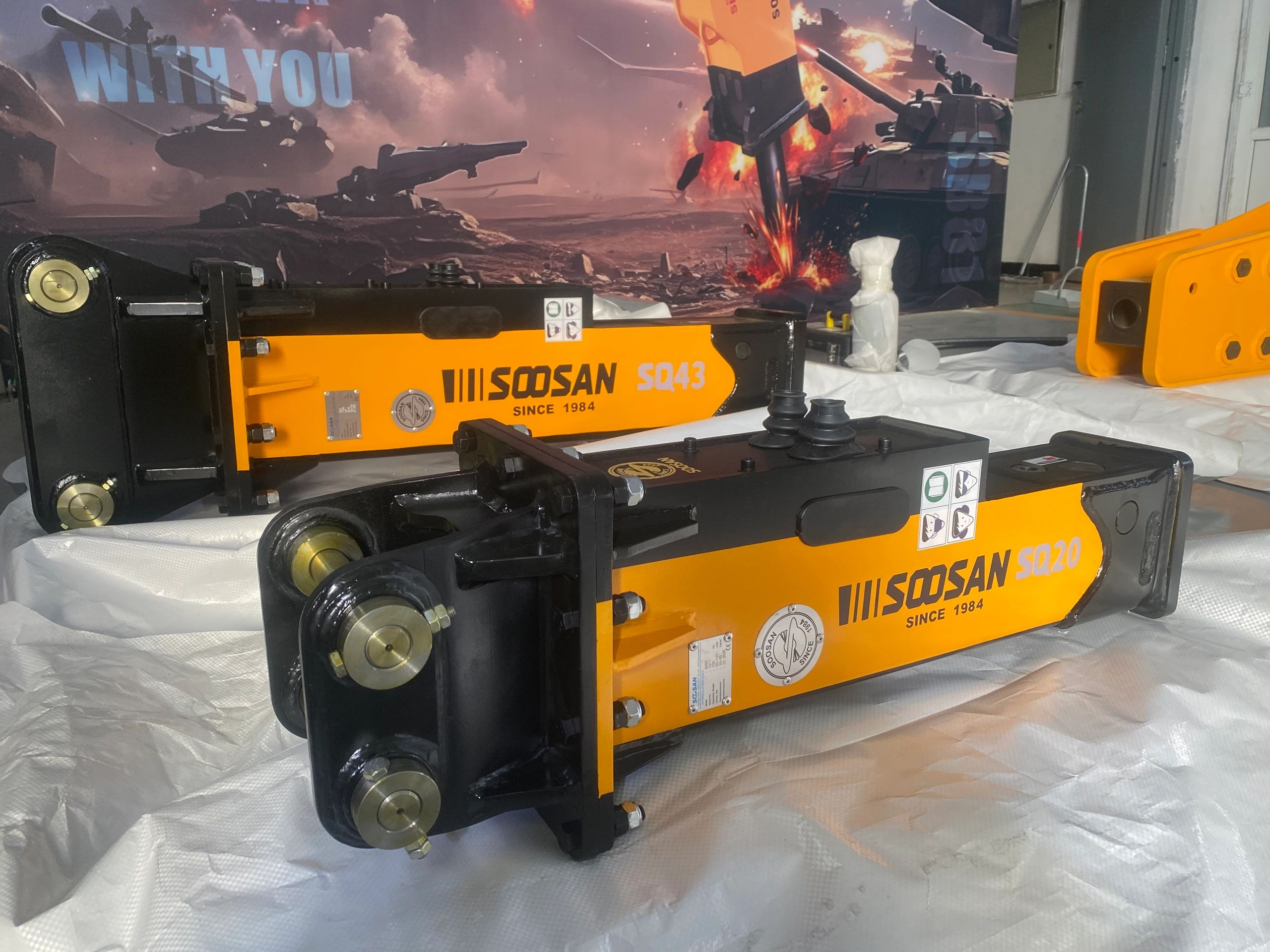 Two yellow and black Soosan hydraulic breakers on a white tarp indoors.