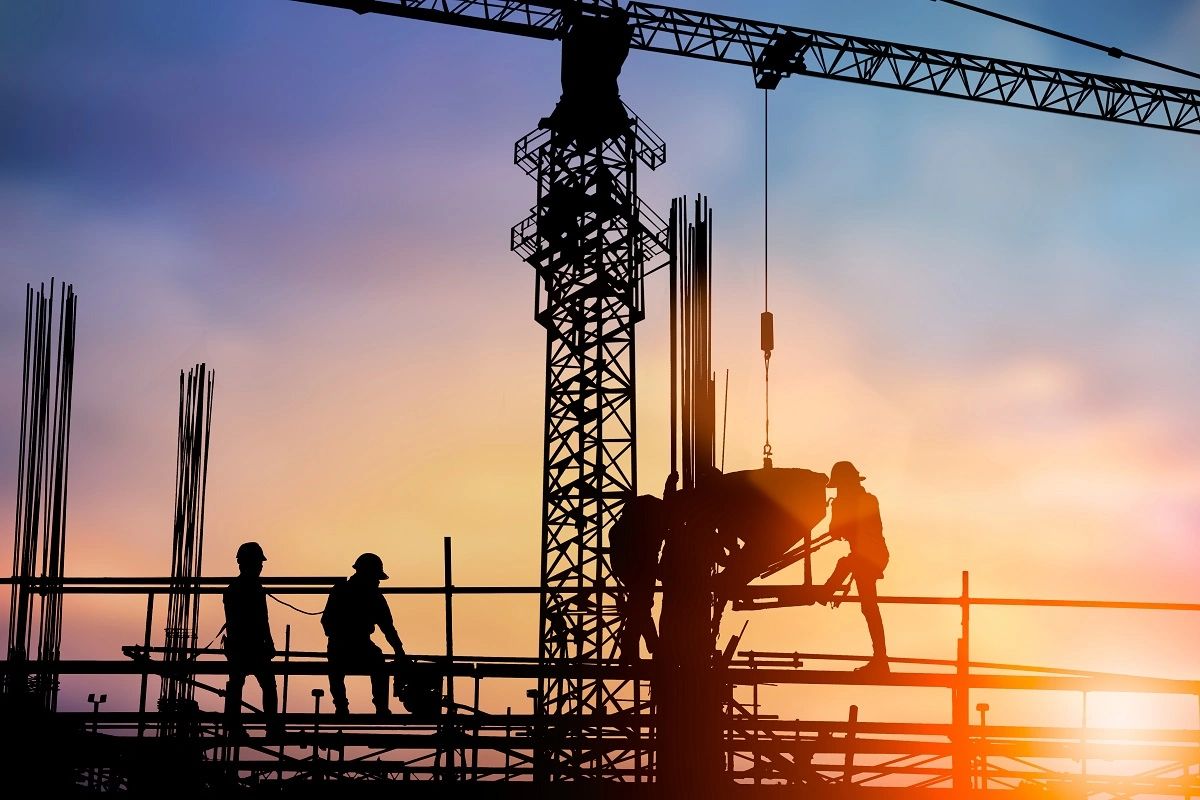 Construction workers with crane at sunset on building site.
