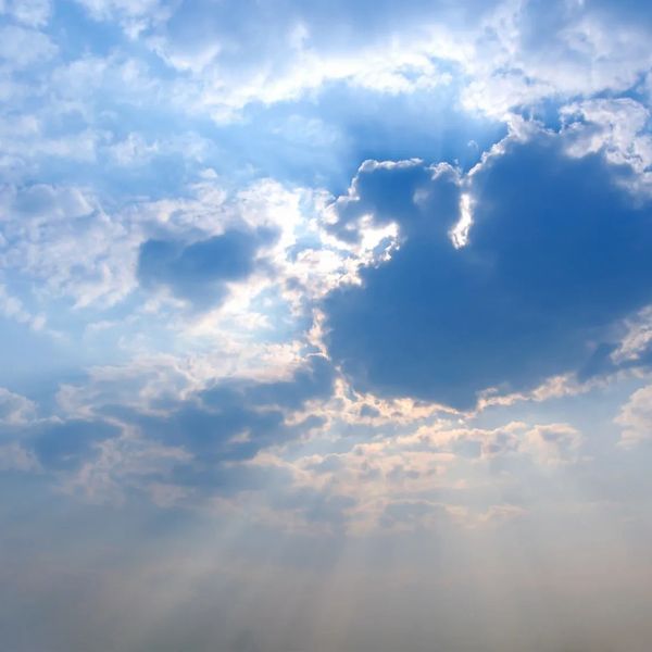 Sunlight peeking through fluffy clouds in a blue sky.