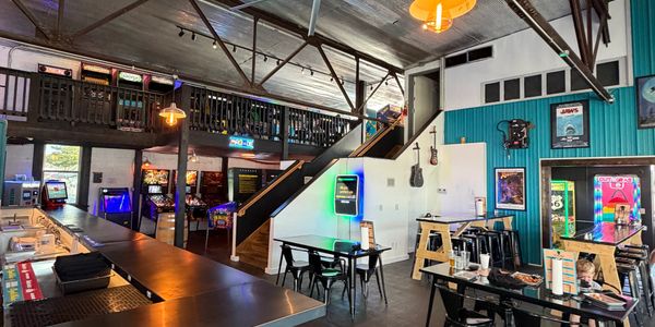 Interior of a retro-style arcade bar with neon lights and vintage posters.