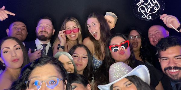 A lively group of friends posing with props and smiles at a party photo booth.