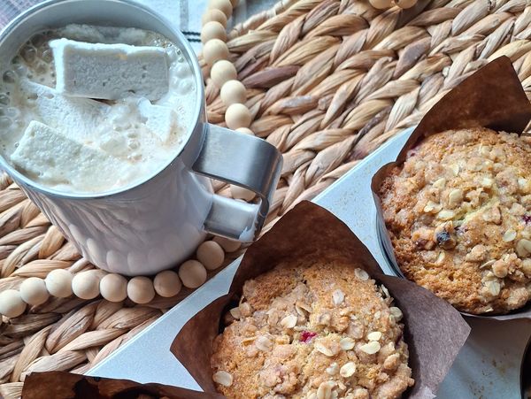 Hot drink with marshmallows and oat-topped muffins on a woven placemat.