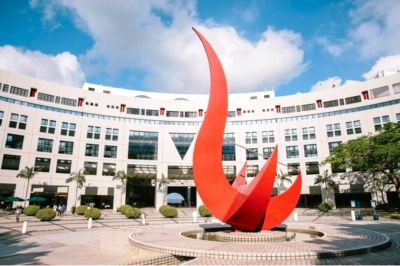 Modern red sculpture in front of a curved white building under a blue sky.