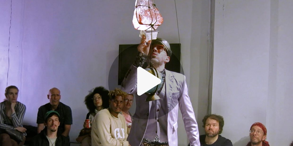 A man in a suit and helmet holding a lamp in front of a seated audience.